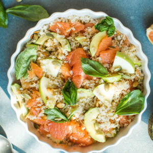 Reissalat mit Grapefruit, Apfel und Avocado in einer weißen geriffelten Form, Draufsicht mit rosa Grapefruit-Filets, Avocado, gerösteten Kürbiskernen und Basilikum