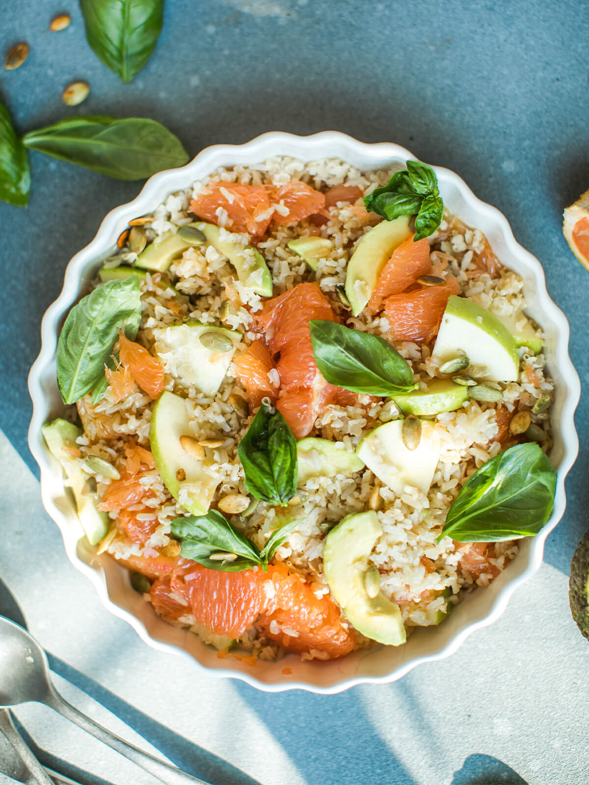 Reissalat mit Grapefruit, Apfel und Avocado in einer weißen geriffelten Form, Draufsicht mit rosa Grapefruit-Filets, Avocado, gerösteten Kürbiskernen und Basilikum