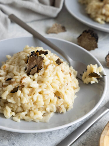 Cremiges Risotto mit Steinpilzen und schwarzem Trüffel auf einem grauen Teller, mit frisch gehobelten Trüffelscheiben obenauf und einer Gabel