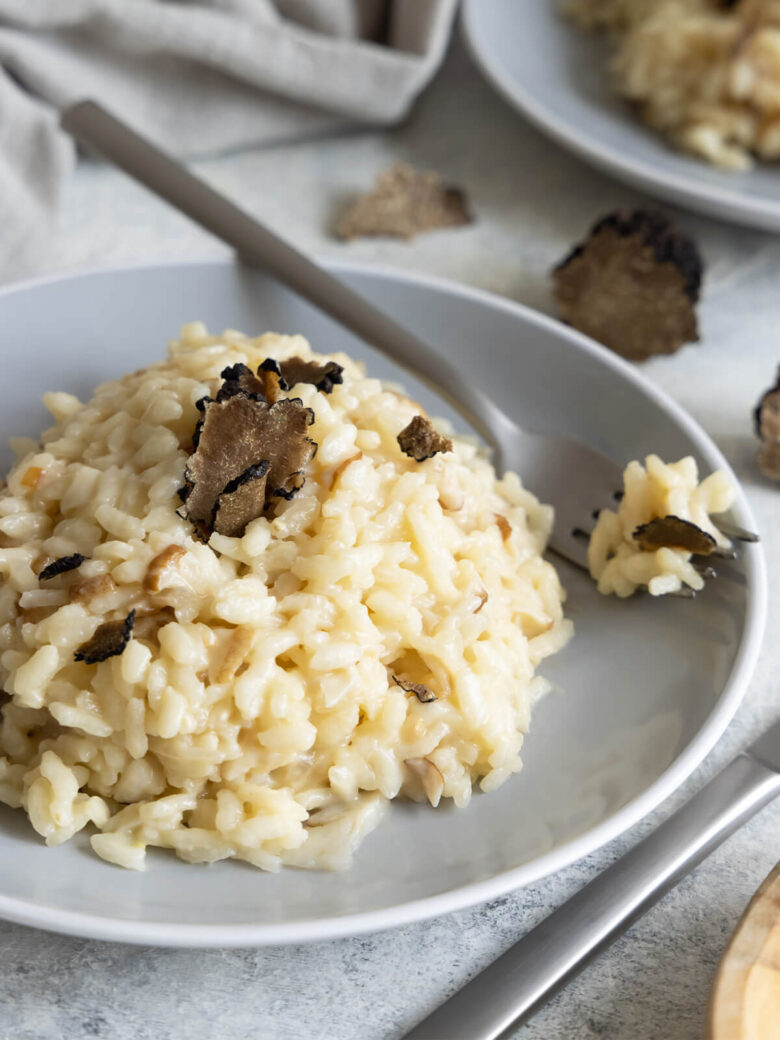 Cremiges Risotto mit Steinpilzen und schwarzem Trüffel auf einem grauen Teller, mit frisch gehobelten Trüffelscheiben obenauf und einer Gabel