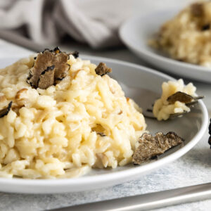 Cremiges Risotto mit Steinpilzen und schwarzem Trüffel auf zwei Tellern, mit gehobelten Trüffelscheiben und Trüffelstücken daneben