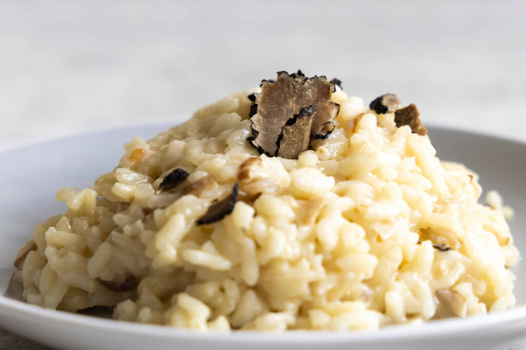 Nahaufnahme eines cremigen Steinpilz-Risottos mit einer prominenten schwarzen Trüffelscheibe und weiteren Trüffelhobeln obenauf