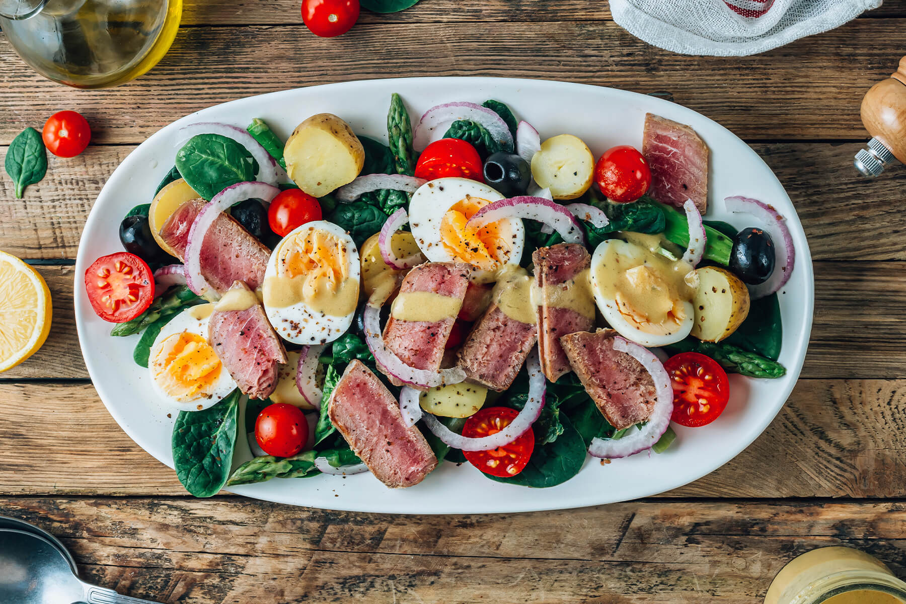 Salade Niçoise mit Thunfisch-Steak in Großaufnahme – rosa Thunfisch-Scheiben, wachsweiche Eierhälften, kleine Kartoffeln und Kirschtomaten mit cremiger Dijon-Vinaigrette
