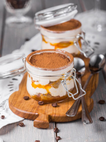 Sanddorn-Tiramisu im Bügelglas mit Kakao bestäubt, weißer Mascarpone-Creme, getränkten Löffelbiskuits und leuchtend orangem Sanddorn-Püree in sichtbaren Schichten