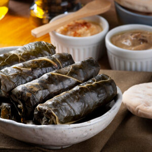 Gefüllte Weinblätter (Sarma) im Schälchen, daneben Hummus und ein weiterer Mezze-Dip mit Fladenbrot