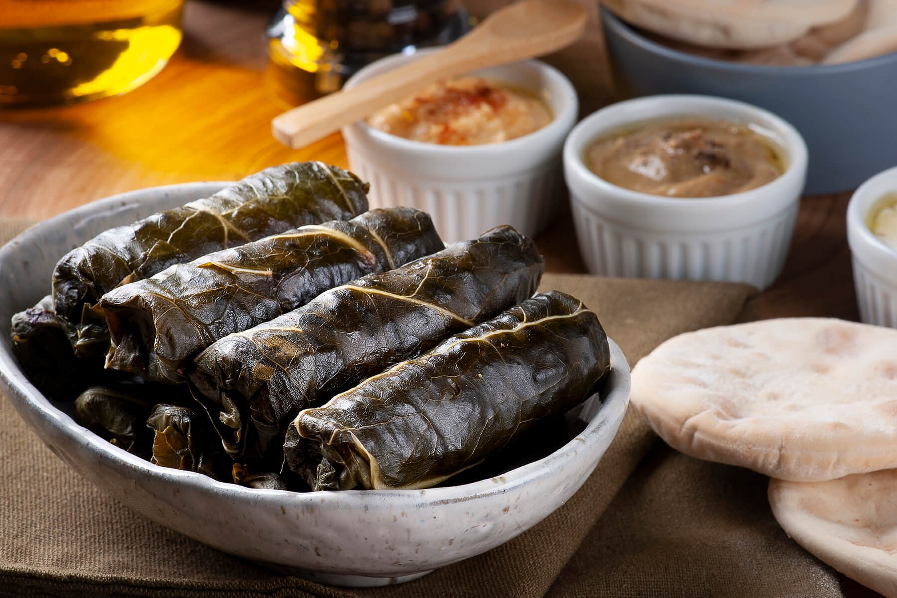 Gefüllte Weinblätter (Sarma) in einer hellen Schale, daneben Hummus und ein weiterer Mezze-Dip mit Fladenbrot