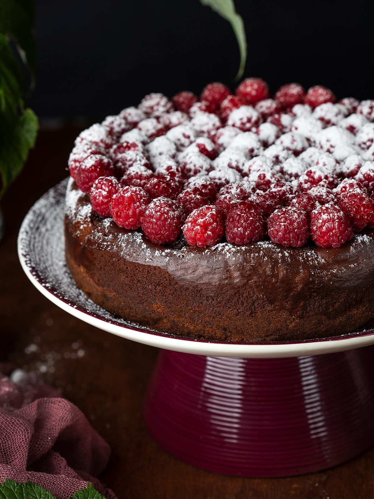 Nahaufnahme der fertigen Schokoladen-Trüffeltorte, frische Himbeeren mit der gewölbten Seite nach oben in konzentrischen Ringen auf der dünnen glänzenden Schokoglasur, rundherum ein schmaler freier Schokorand