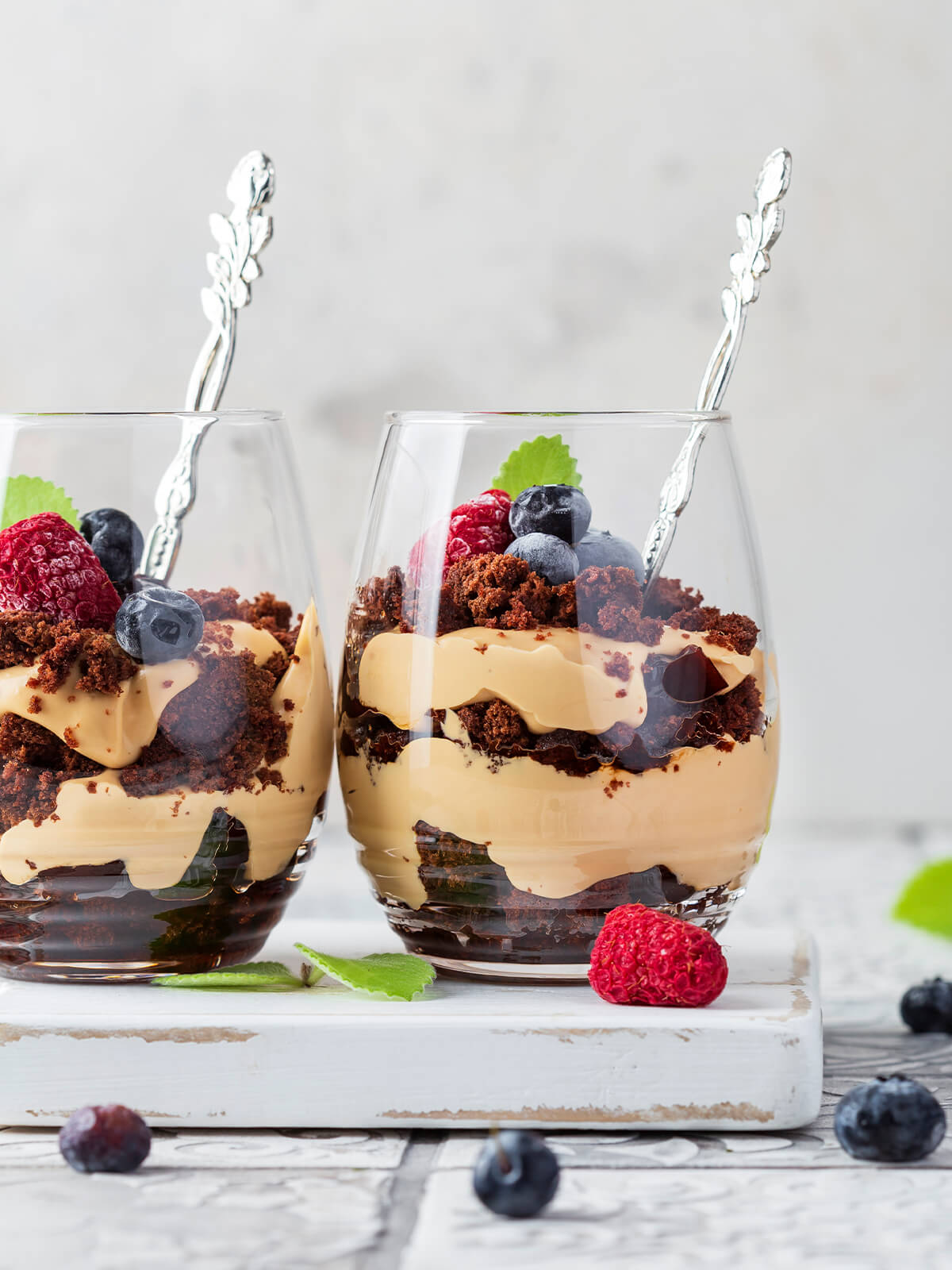 Zwei Gläser mit Schoko-Karamell-Schichtdessert nebeneinander, deutlich sichtbare Schichten aus dunklen Schokobröseln und karamellfarbener Mascarpone-Creme, oben frische Beeren