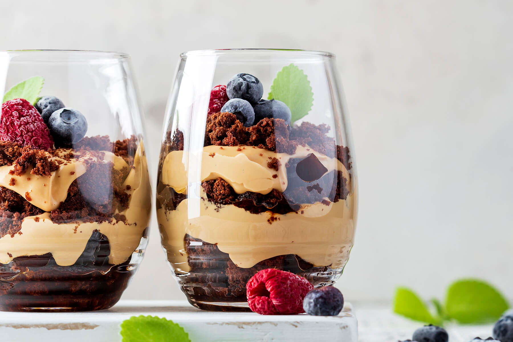 Zwei Gläser Schoko-Karamell-Schichtdessert auf Augenhöhe fotografiert, deutlich sichtbare abwechselnde Schichten aus Schokobröseln und karamellfarbener Creme bis zum Glasboden