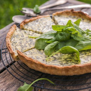 Klassische Spinat-Quiche auf einem schwarzen Kuchengitter, in der Mitte mit frischen Spinatblättern garniert