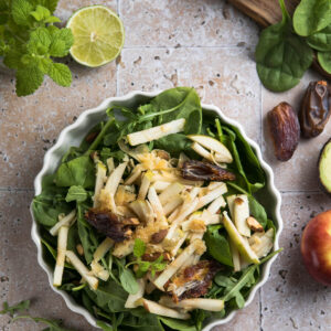 Spinatsalat mit Apfel, Datteln und Mandeln von oben in einer geriffelten cremeweißen Servierform mit hellem Zitrus-Dressing