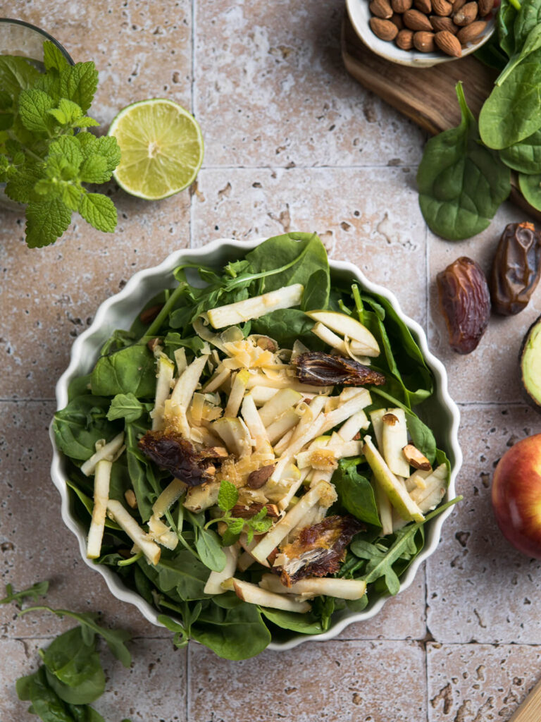 Spinatsalat mit Apfel, Datteln und Mandeln von oben in einer geriffelten cremeweißen Servierform mit hellem Zitrus-Dressing