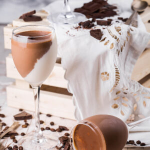 Schoko-Vanille-Panna-Cotta im Stielglas mit diagonaler Trennlinie zwischen weißer Vanille- und brauner Schokoladenschicht, daneben Schokoladenstücke und Kaffeebohnen
