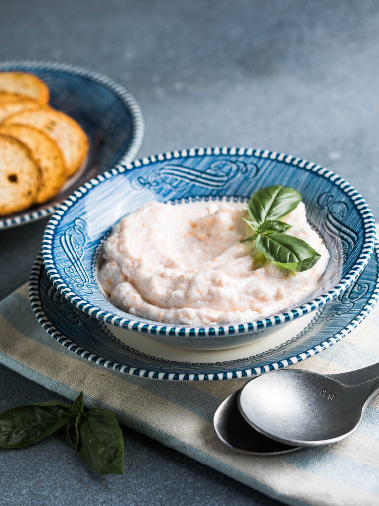 Griechische Taramosalata mit körniger Struktur in einer blau gemusterten Schale, daneben eine Schale mit goldbraun gerösteten Brotscheiben