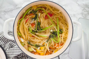 Spaghetti köcheln offen im Topf mit Kirschtomaten, Zwiebel und Basilikum, die Flüssigkeit kocht langsam ein