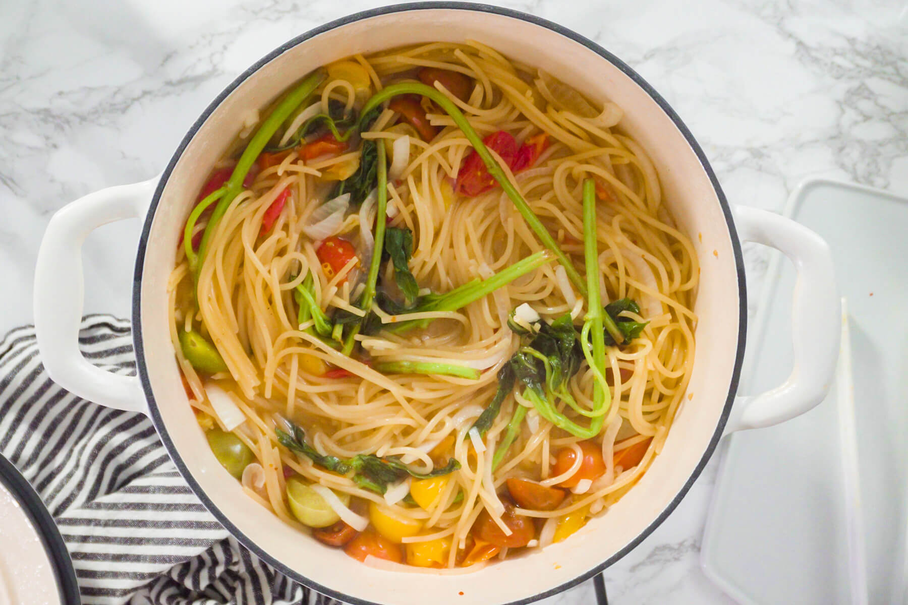Spaghetti köcheln offen im Topf mit Kirschtomaten, Zwiebel und Basilikum, die Flüssigkeit kocht langsam ein