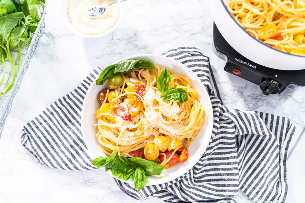 Vegetarische One-Pot-Pasta mit Spaghetti, bunten Kirschtomaten, geriebenem Hartkäse und frischem Basilikum in einer weißen Schale
