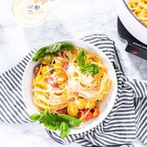 Vegetarische One-Pot-Pasta mit Spaghetti, bunten Kirschtomaten, geriebenem Hartkäse und frischem Basilikum in einer weißen Schale