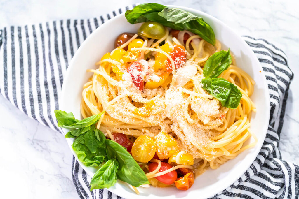 Vegetarische One-Pot-Pasta mit Spaghetti, bunten Kirschtomaten, geriebenem Hartkäse und frischem Basilikum in einer weißen Schale