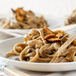 Vollkorn-Tagliolini mit gebratenen Steinpilzen in cremiger Sahnesauce auf weißem Teller