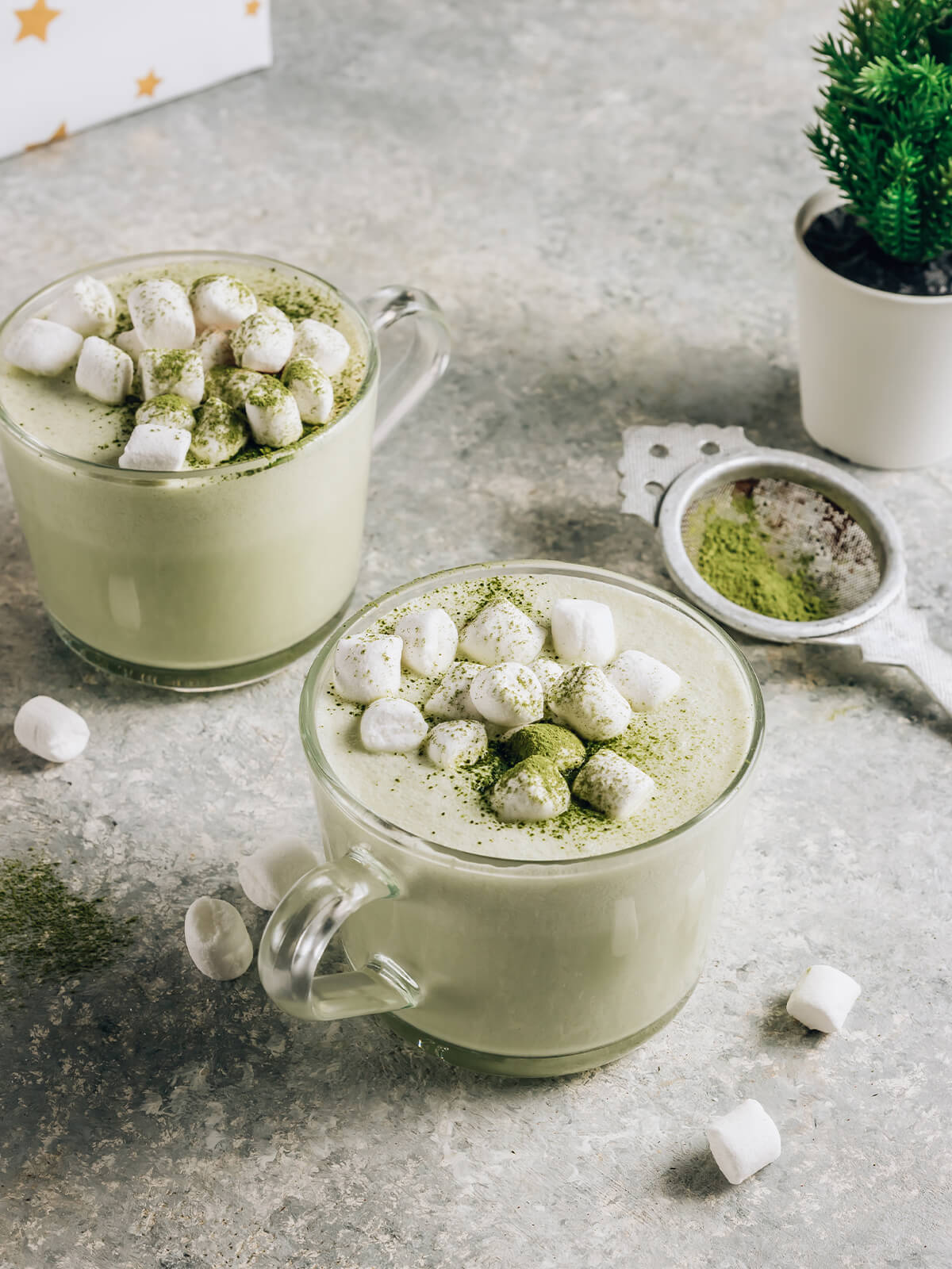 Zwei Gläser warmer Matcha-Latte mit Kokosmilch, belegt mit Mini-Marshmallows und mit grünem Matcha bestäubt