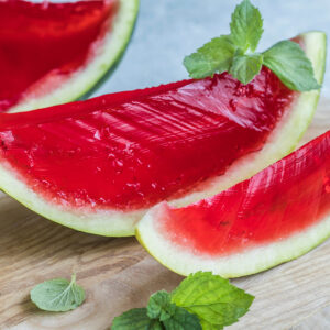 Drei Spalten Wassermelonen-Gelee mit grüner Schale und klarem rubinrotem Gelee, dekoriert mit Minzblättern auf einem Holzbrett