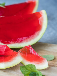 Angeschnittene Wassermelonenhälfte mit rubinrotem Gelee, davor zwei kleinere Endstücke mit heller Schale und klarem rotem Gelee