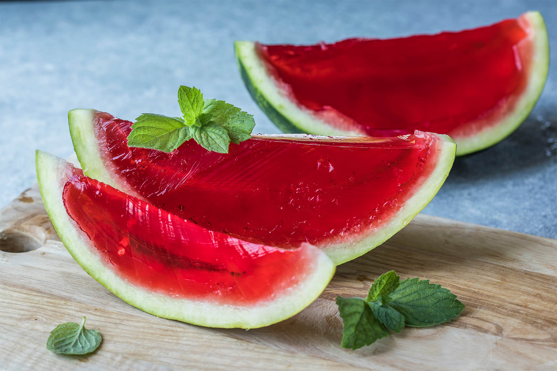 Mehrere Spalten Wassermelonen-Gelee mit klarem rubinrotem Inneren und grüner Schale, garniert mit frischer Minze auf einem Holzbrett