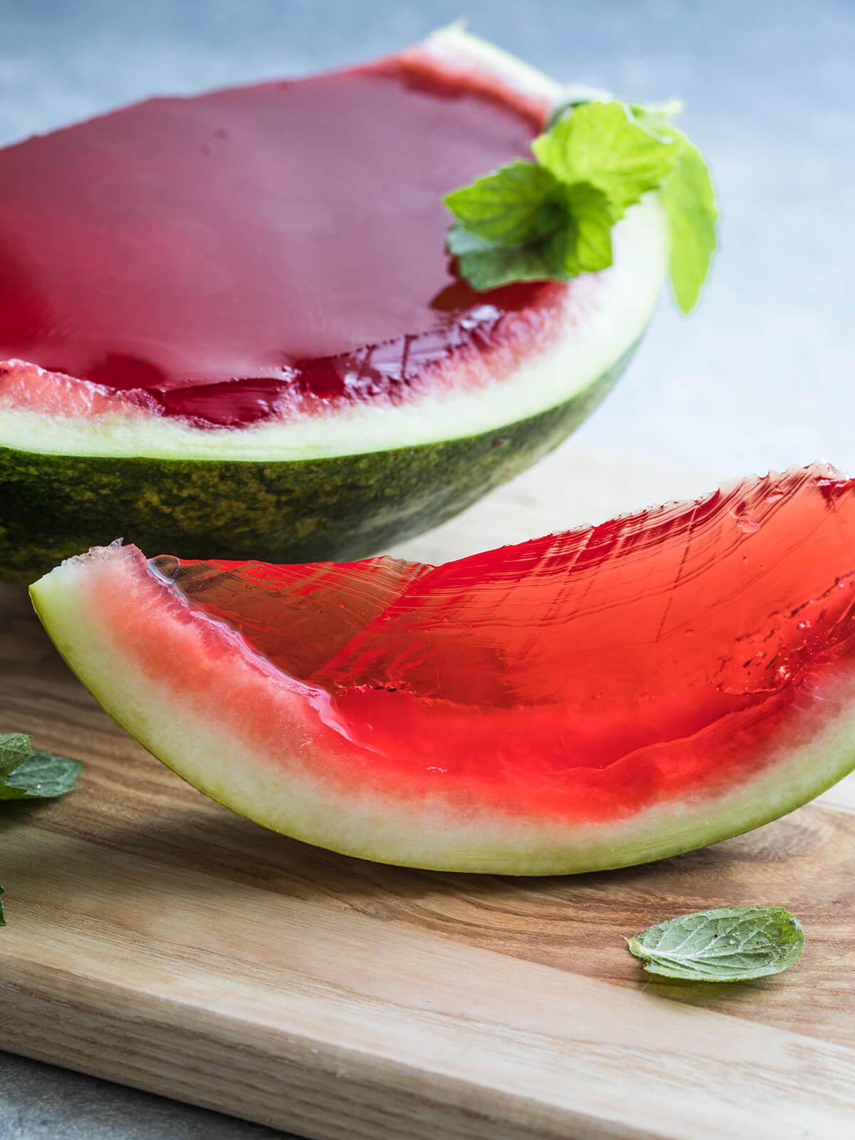 Ausgehöhlte Wassermelonenhälfte gefüllt mit fest gewordenem dunkelrotem Gelee, daneben eine bereits geschnittene Spalte und Minzblätter