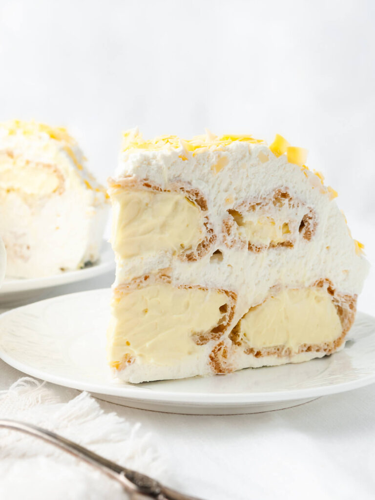 Stück Windbeuteltorte mit hohlen Brandteig-Windbeuteln, heller Vanillecreme und viel Schlagsahne, im Anschnitt auf einem weißen Teller