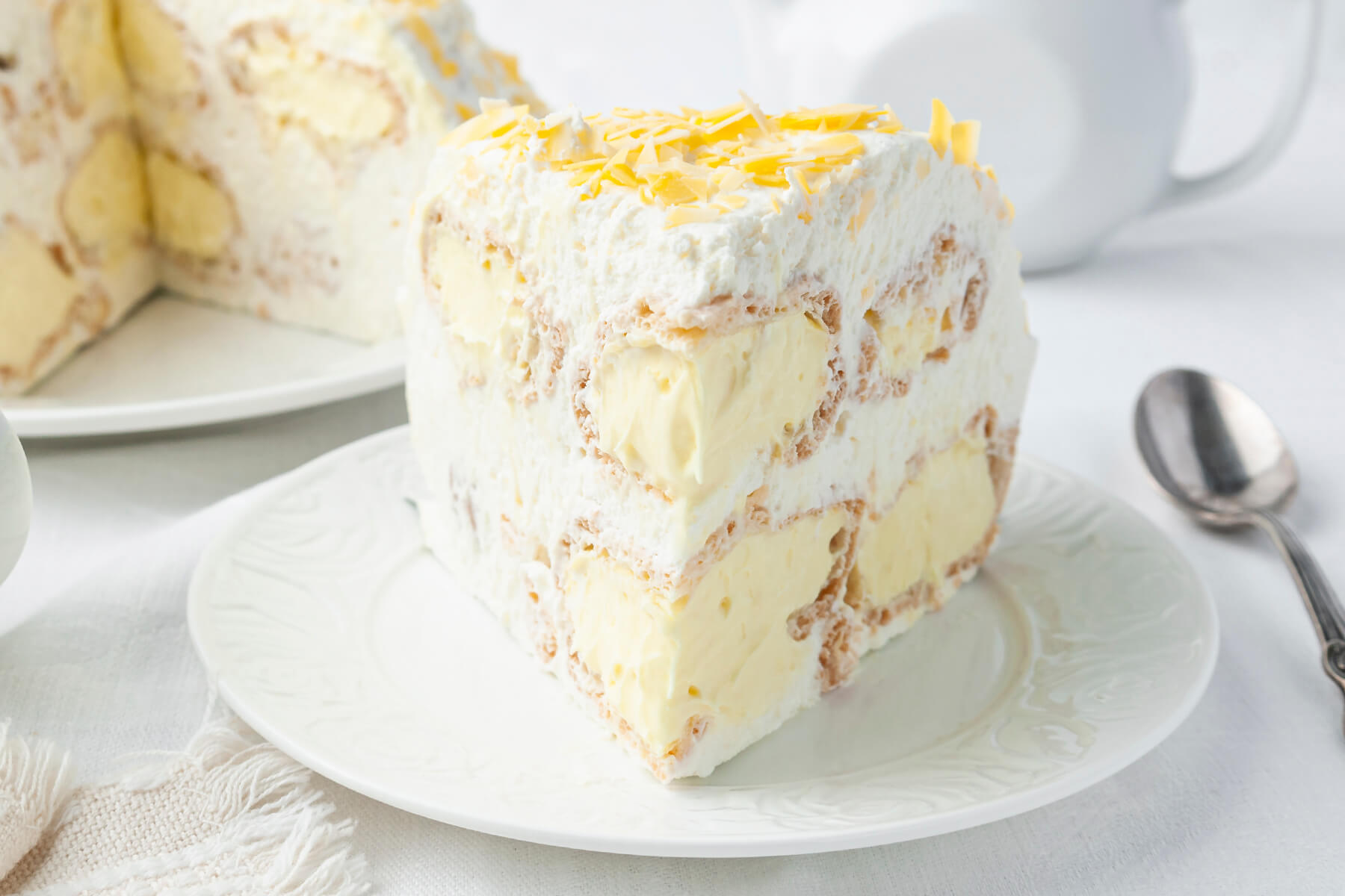 Nahaufnahme eines Stücks Windbeuteltorte mit deutlich sichtbaren hohlen Windbeuteln, Vanillecreme, Schlagsahne und weißen Schokoladenspänen