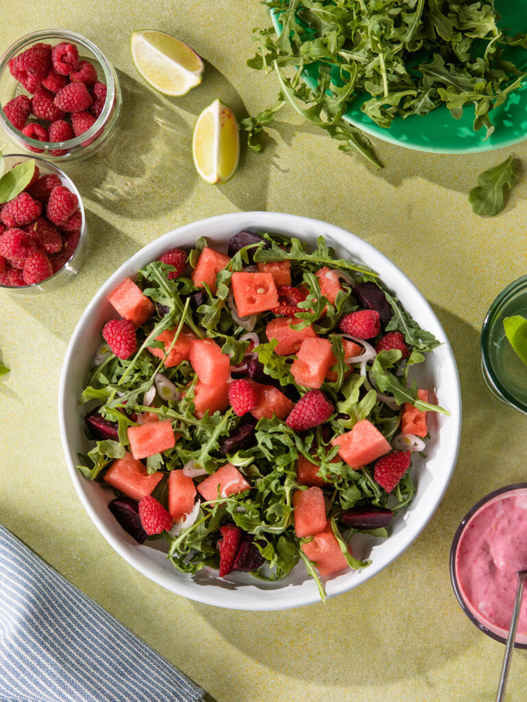 Veganer Wassermelonen-Rucola-Salat mit Himbeeren, Rote Bete und rosa Himbeer-Dressing in einer weiΓen Schale, von oben fotografiert