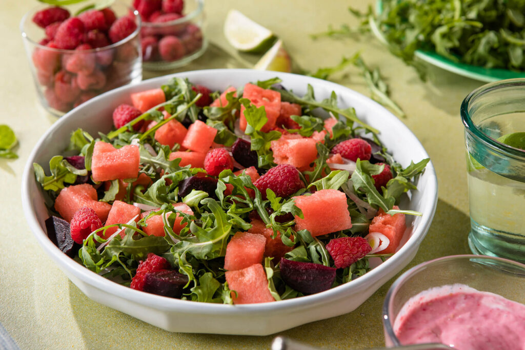 Veganer Wassermelonen-Rucola-Salat mit Himbeeren, Rote Bete und rosa Himbeer-Dressing in einer weiΓen Schale aus der NΓ€he