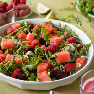 Veganer Wassermelonen-Rucola-Salat mit Himbeeren, Rote Bete und rosa Himbeer-Dressing in einer weiΓen Schale aus der NΓ€he