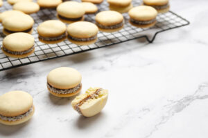 Fertige Alfajores de Maicena mit Kokosrand auf einem Kuchengitter, davor ein aufgebrochenes Stück mit sichtbarer Füllung