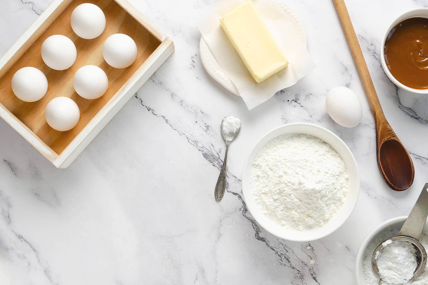 Zutaten für Alfajores de Maicena – Eier, Butter, Maisstärke, Mehl und Dulce de Leche auf Marmor