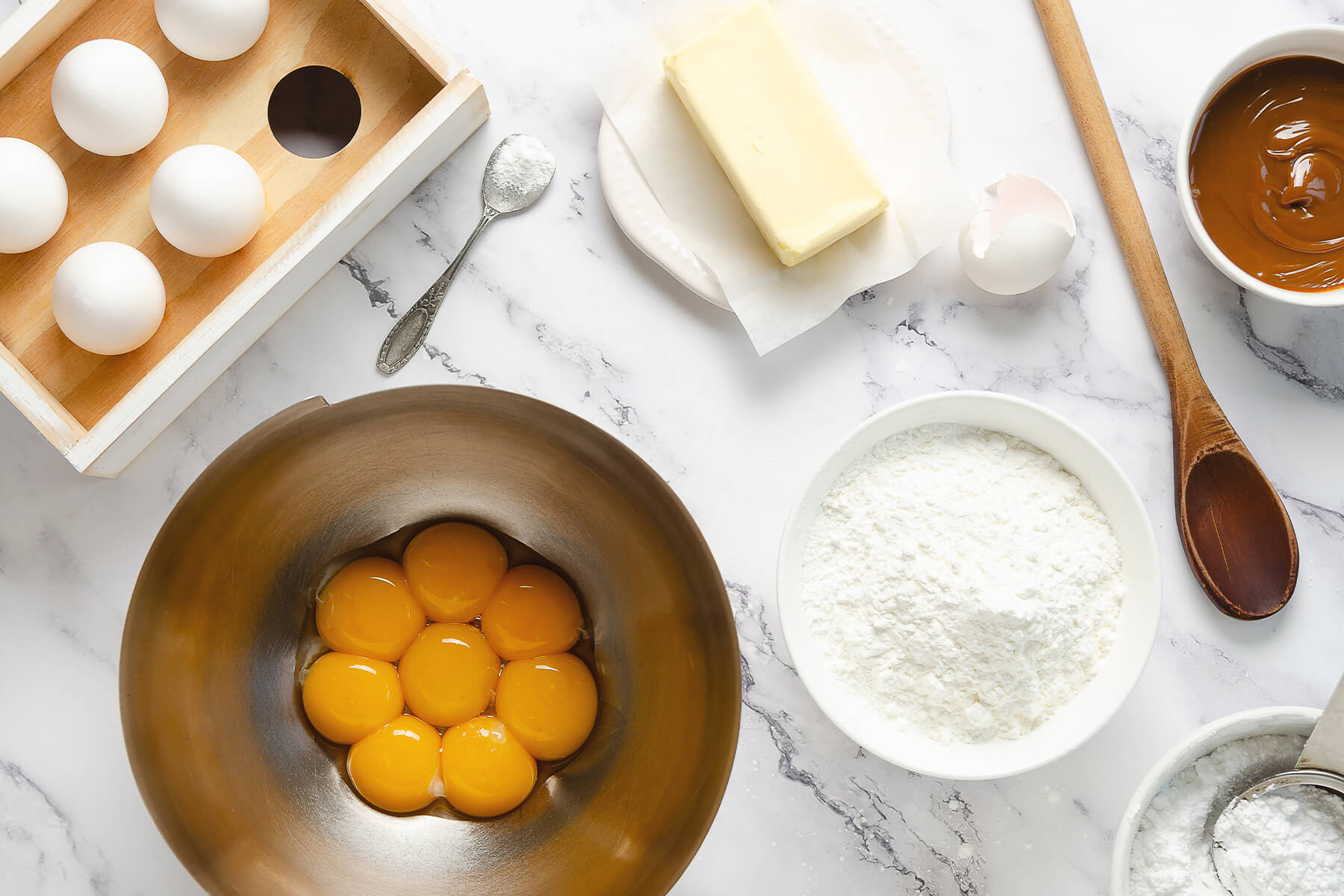 Eigelbe in einer Metallschüssel neben Maisstärke, Mehl und Dulce de Leche