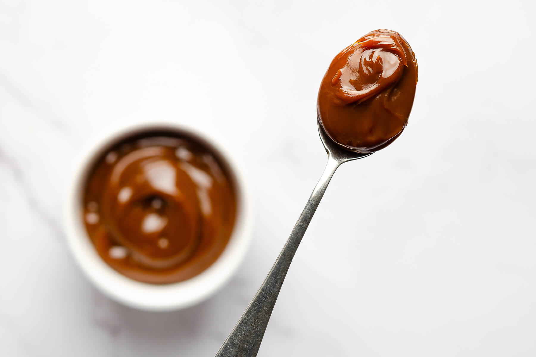 Ein Löffel mit dickem, glänzendem Dulce de Leche über einer kleinen Schale