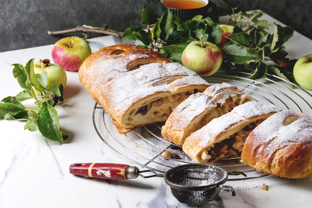 Angeschnittener Apfelstrudel aus Hefeteig mit sichtbarer Apfel-Rosinen-Füllung, bestäubt mit Puderzucker