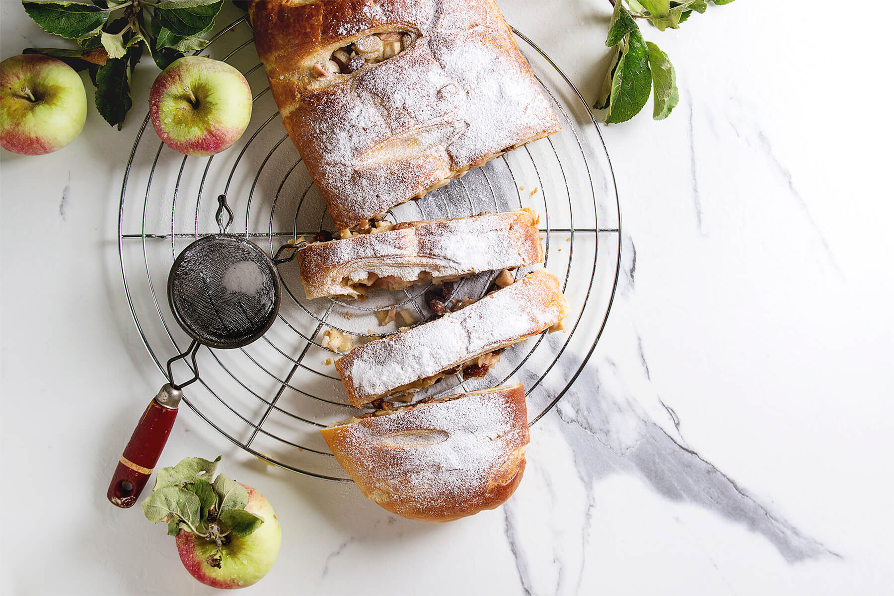 Apfelstrudel aus Hefeteig in Scheiben von oben auf einem runden Kuchengitter, bestäubt mit Puderzucker