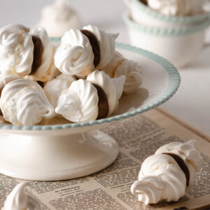 Weisse Baiser-Doppelkekse mit Dulce-de-Leche-Fuellung auf einer Kuchenetagere mit mintgruenem Rand