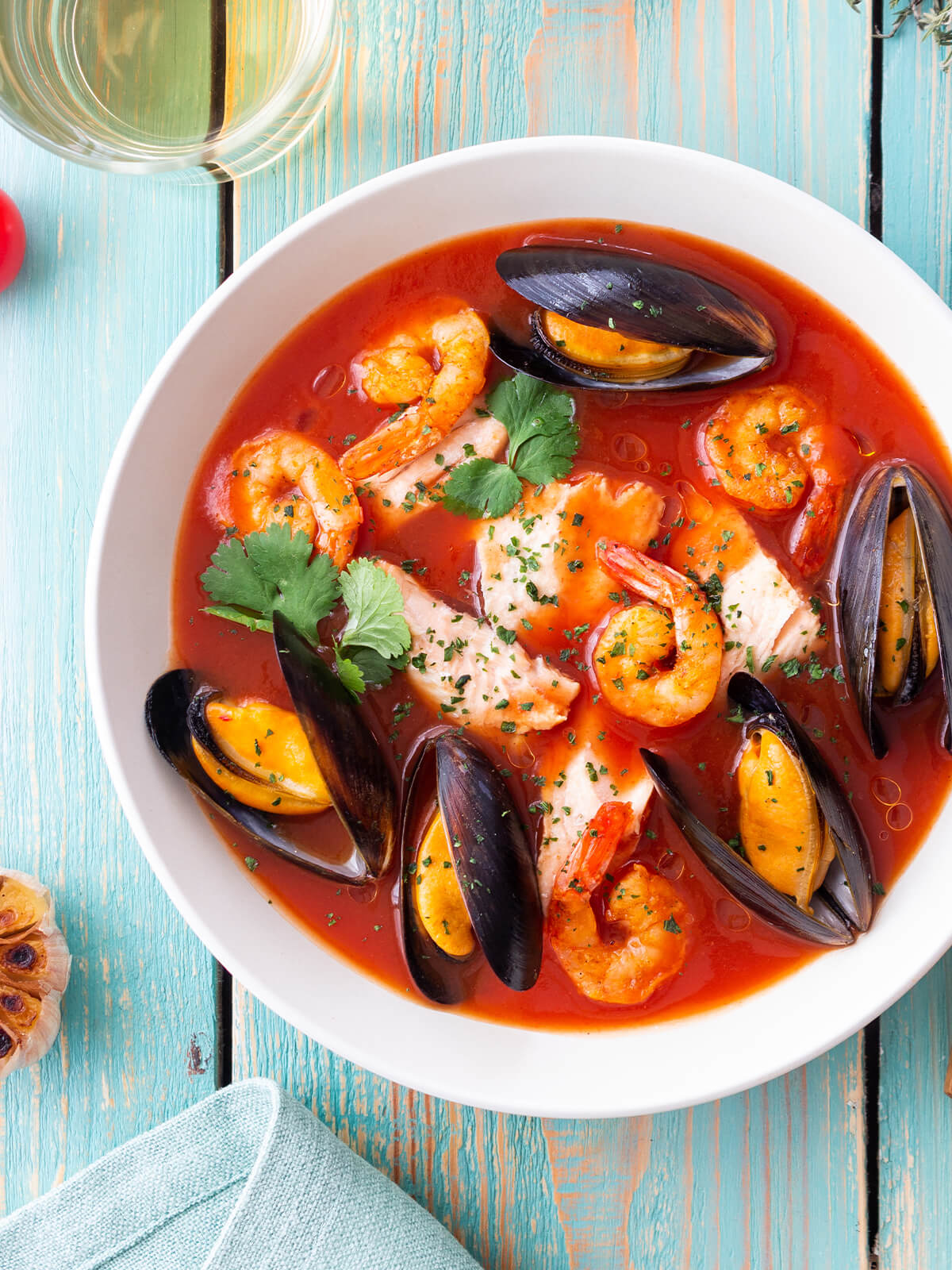 Französische Bouillabaisse mit Fisch, Miesmuscheln und Garnelen in roter Brühe in einem weißen Teller von oben