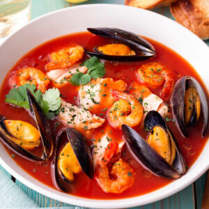 Französische Bouillabaisse mit Fisch, Miesmuscheln und Garnelen in roter Brühe in einem weißen Teller, dazu Baguette