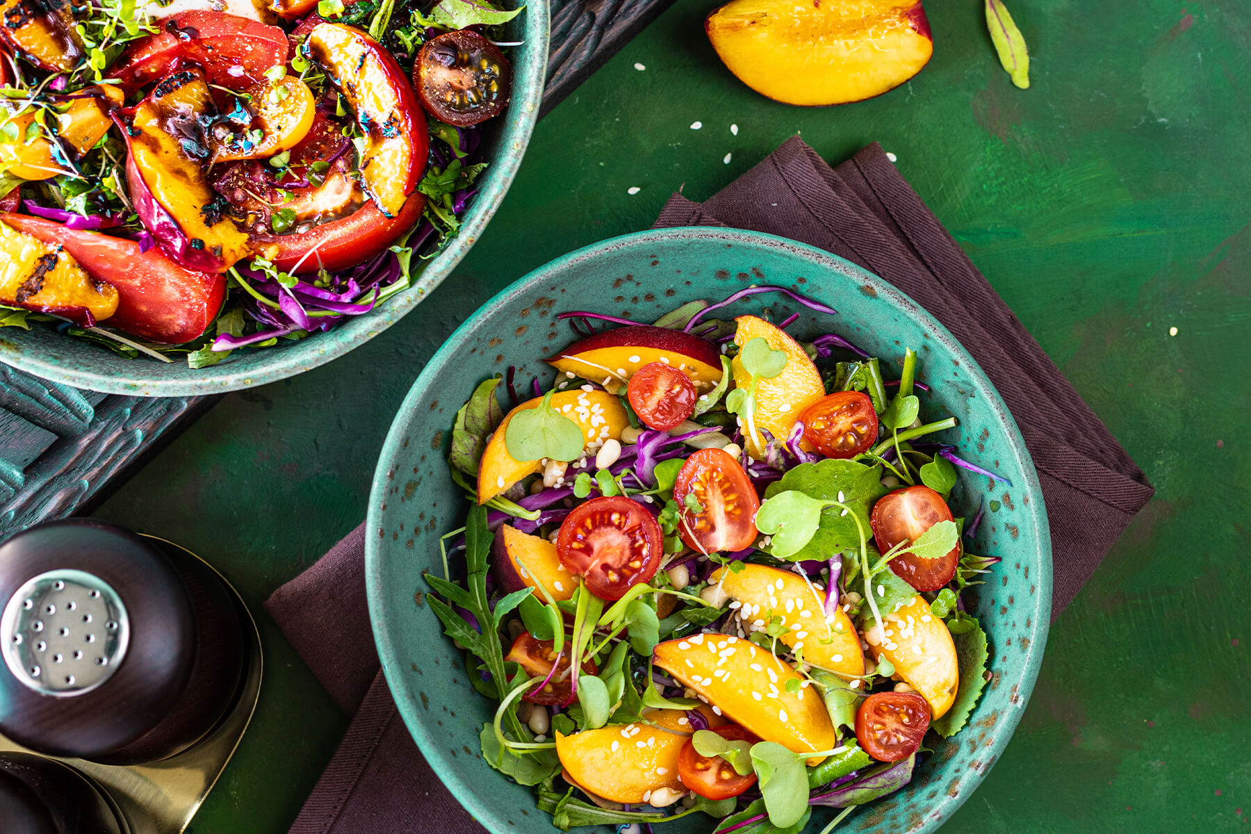 Zwei türkisfarbene Keramikschalen mit Sommersalat von oben; im Vordergrund die Variante ohne Burrata mit rohen Nektarinenspalten, halbierten Kirschtomaten, fein gehobeltem Rotkohl, Rucola, Microgreens sowie hellem Sesam und Pinienkernen, oben links vom Bildrand angeschnitten und nur teilweise sichtbar die zweite Schale mit gegrillten Nektarinenspalten, Fleischtomaten und dunkler Balsamico-Creme