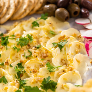Butter Board mit in Wellen gestrichener Butter, Walnüssen und Petersilie, umgeben von Crackern, Oliven und Radieschen