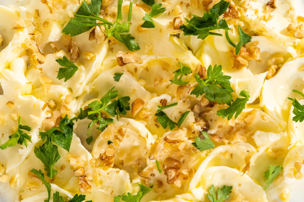 Nahaufnahme von in Wellen gestrichener Butter mit gerösteten Walnüssen, Petersilie und einem Faden Olivenöl