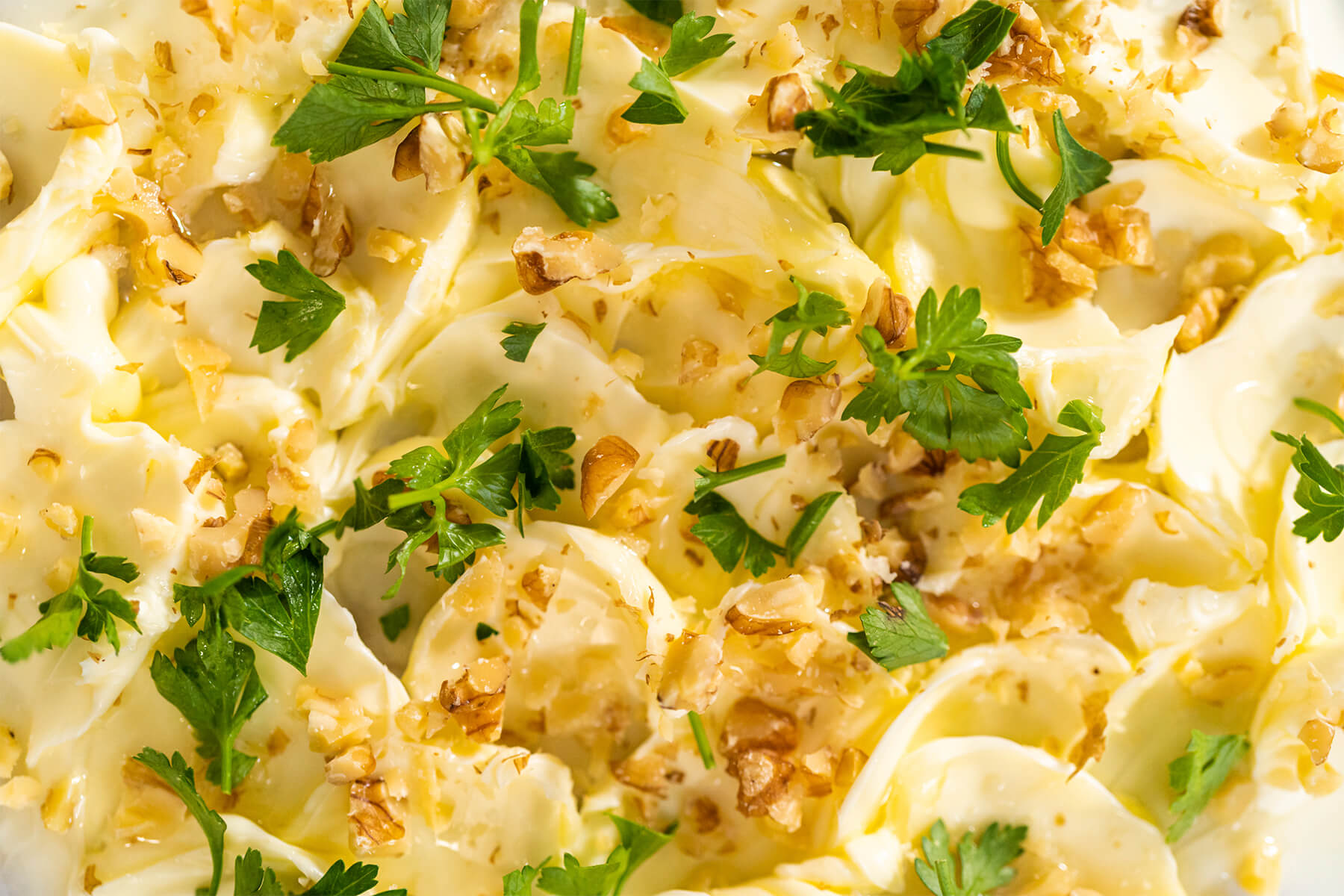 Nahaufnahme von in Wellen gestrichener Butter mit gerösteten Walnüssen, Petersilie und einem Faden Olivenöl