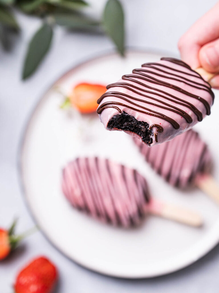 Angebissenes Schoko-Cakesicle in einer Hand, der tiefdunkle Kuchenkern ist sichtbar