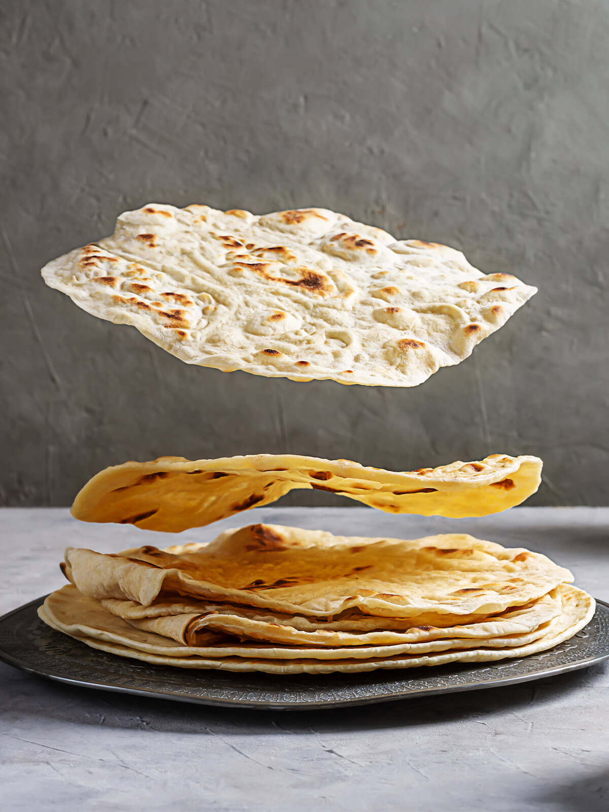 Indische Chapati-Fladenbrote, teils in der Luft schwebend über einem Stapel auf einem verzierten Metallteller