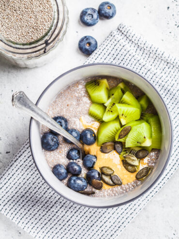 Veganer Chia-Pudding aus weißen Chiasamen mit Kiwistücken, Blaubeeren, Erdnussmus und Kürbiskernen in einer grauen Schale von oben